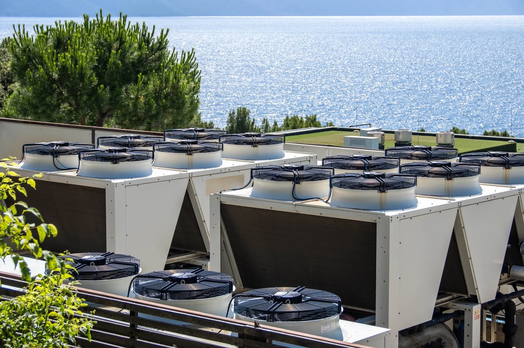 Unidades industriales de climatización o producción térmica instaladas en una cubierta exterior, con múltiples ventiladores superiores y vistas al mar al fondo. La instalación está rodeada de vegetación y ubicada en un entorno costero.