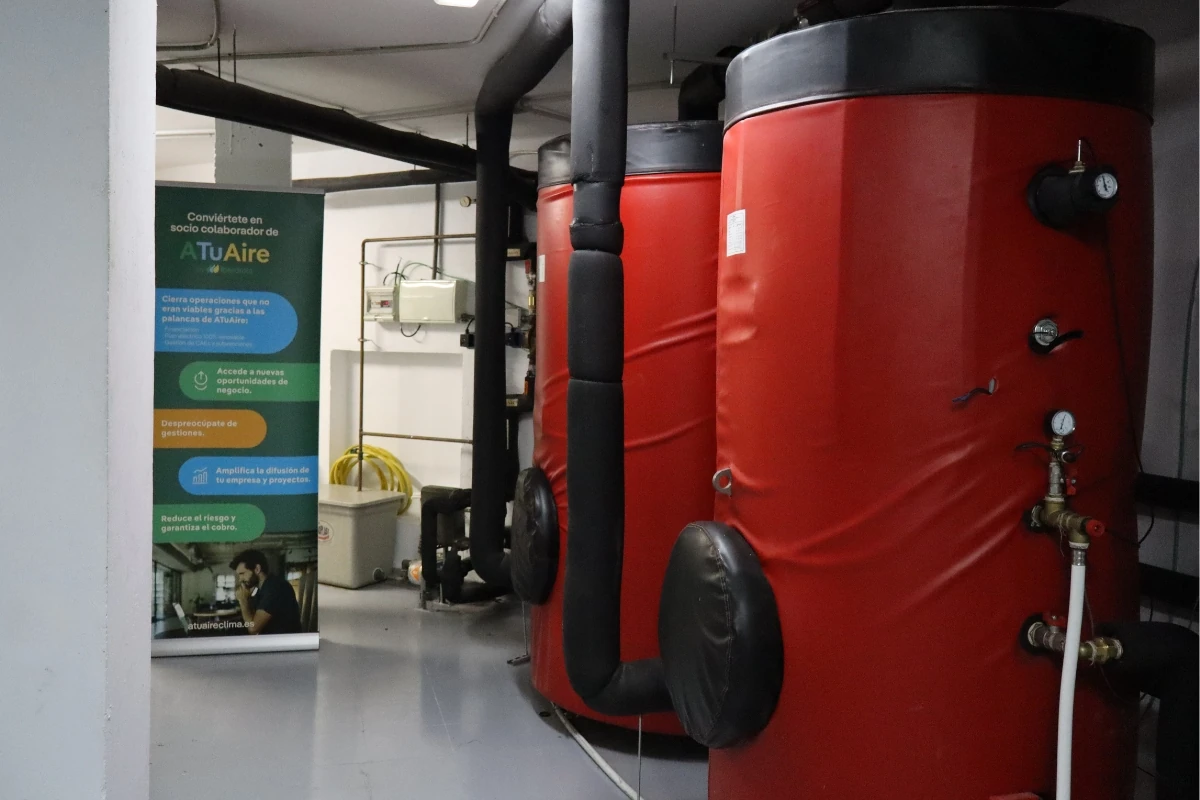 Sala técnica con varios depósitos acumuladores térmicos de gran capacidad revestidos en color rojo, conectados mediante tuberías aisladas. Al fondo se observa un panel informativo de ATuAire by Iberdrola.