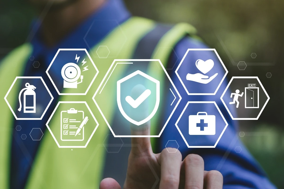 Ilustración sobre seguridad laboral y prevención de riesgos que muestra diversos iconos relacionados con protección, emergencias, primeros auxilios y control de seguridad. En el centro destaca un escudo con una marca de verificación sobre una persona con chaleco de alta visibilidad al fondo.