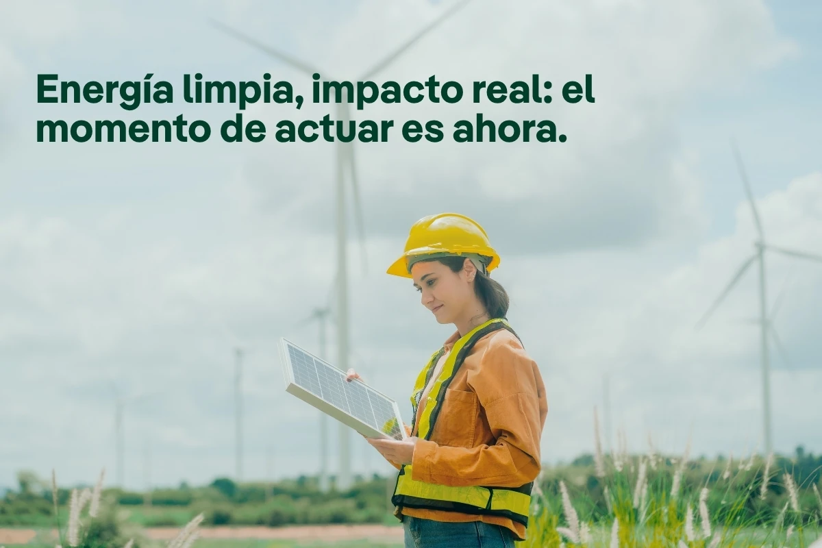 Imagen promocional sobre energía limpia y sostenibilidad que muestra a una persona con casco de seguridad sosteniendo un panel solar en un entorno con aerogeneradores al fondo. En la parte superior aparece el mensaje: “Energía limpia, impacto real: el momento de actuar es ahora”.