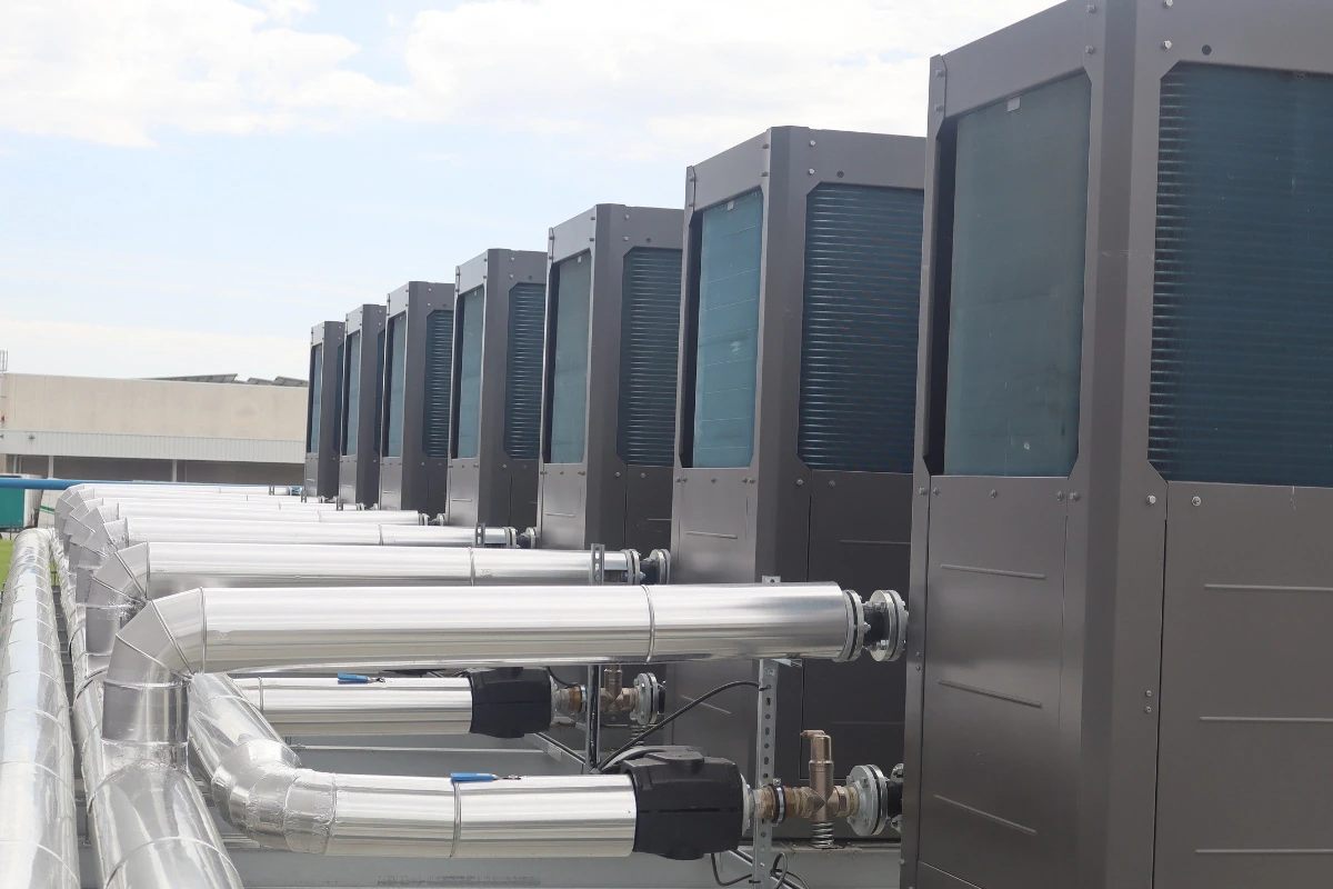 Fila de unidades exteriores de climatización o bombas de calor colocadas sobre la azotea de una instalación industrial, conectadas a un sistema hidráulico mediante conductos y tuberías aisladas.