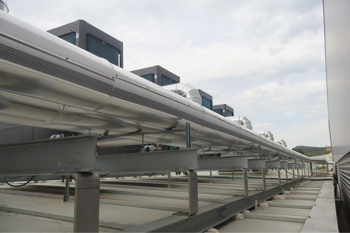 Red de tuberías metálicas aisladas montadas sobre una estructura elevada en la cubierta de un edificio, conectadas a equipos de climatización para el transporte de agua o energía térmica.