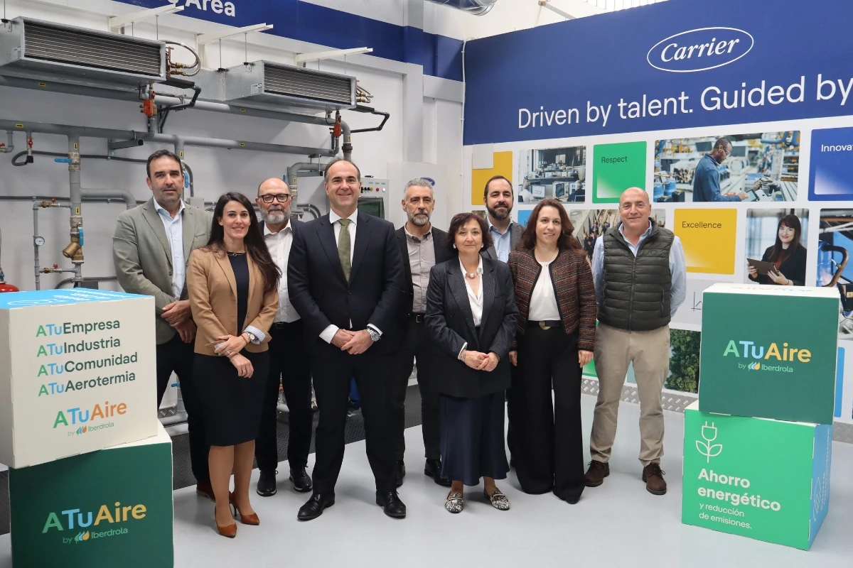 Fotografía de grupo tomada en un espacio de formación técnica e innovación en climatización. Varias personas posan frente a equipos de refrigeración y climatización, junto a elementos corporativos de ATuAire by Iberdrola y paneles informativos de Carrier.