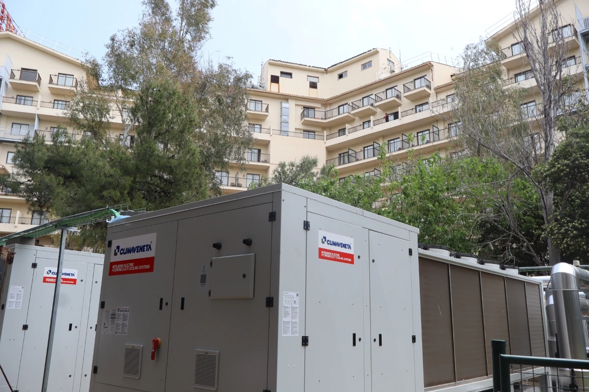 Instalación exterior de climatización y producción térmica compuesta por unidades industriales de gran capacidad ubicadas junto a un edificio hotelero rodeado de árboles y vegetación.