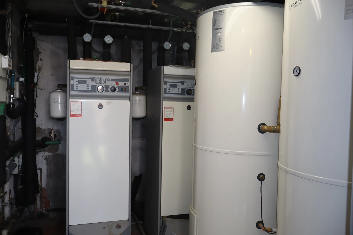 Sala técnica con equipos de producción de agua caliente y calefacción, formada por calderas, depósitos acumuladores verticales e instrumentos de control conectados a la instalación hidráulica.