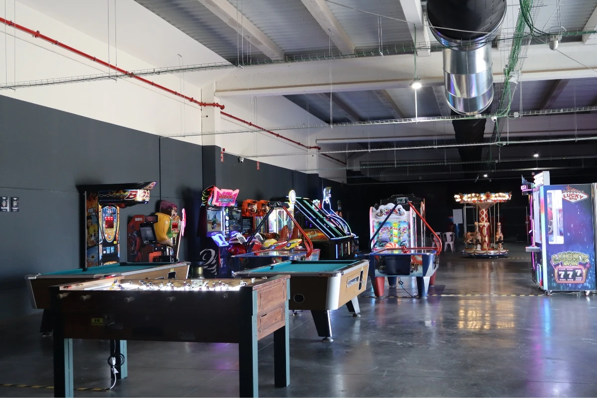 Espacio interior de entretenimiento con mesas de billar, máquinas recreativas y juegos arcade distribuidos en una amplia sala iluminada.