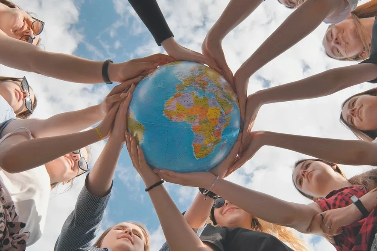 Grupo de personas sosteniendo conjuntamente un globo terráqueo al aire libre, formando un círculo alrededor del planeta como símbolo de colaboración, sostenibilidad y compromiso con el medioambiente.